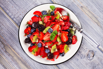 Strawberry, blackberry, blueberry and kiwi salad, garnished with mint. Fruit and berry salad. View from above, top studio shot