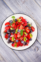 Strawberry, blackberry, blueberry and kiwi salad, garnished with mint. Fruit and berry salad. View from above, top studio shot