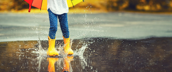 Feet of  child in yellow rubber boots jumping over  puddle in rain - obrazy, fototapety, plakaty