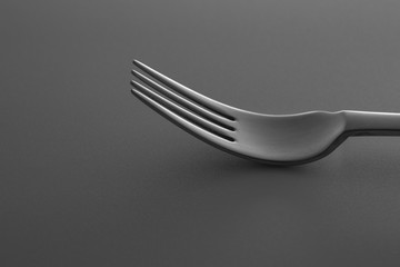 Close-up shot of metallic fork lying down on dark gray surface. Minimalistic design photo.
