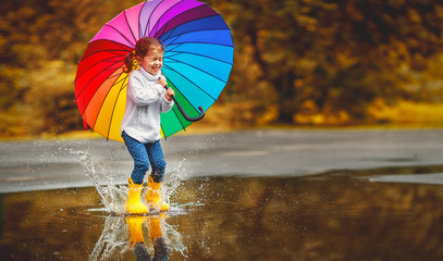 Happy funny child girl with  umbrella jumping on puddles in rubber boots  .