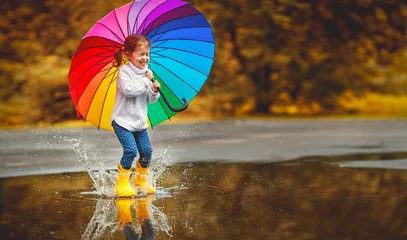 Fotobehang Happy funny child girl with  umbrella jumping on puddles in rubber boots  . © JenkoAtaman