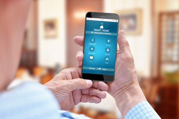 Old man using smartphone for controlling smart home system while sitting in living room