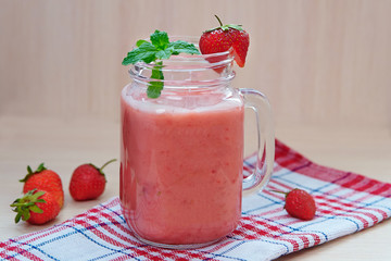 Strawberry smoothies in a glass jar, berries, and mint on a towel in a cage