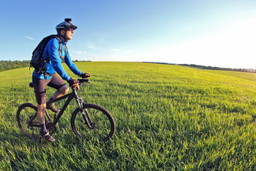 cyclist rides a bicycle on the green field towards the sun