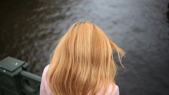 A woman in a coat stands on a bridge and looks down at the black water. She wants to commit suicide