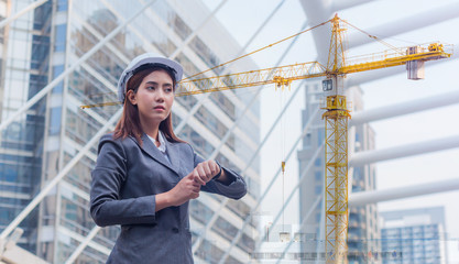 Portrait of beautiful young engineer woman wear a white safety helmet waiting times at downtown with building background