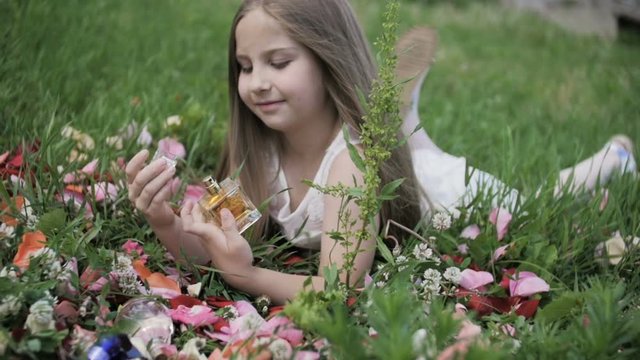 The girl lies in the grass and looks at the perfume bottles.