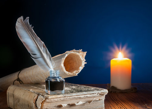 Quill pen and a rolled papyrus sheet on an old book by candle light