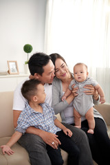 Portrait of young Asian family playing with adorable little kids at home, sitting on sofa