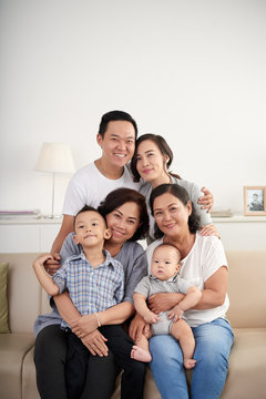 Portrait of big Asian family posing for photo at home sitting on sofa, all smiling happily looking at camera