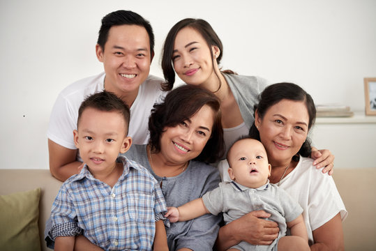 Portrait of  big Asian family with two children posing for photo at home, all smiling happily looking at camera