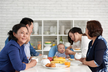 Portrait of mature Asian woman sitting at dining table with big family and smiling to camera