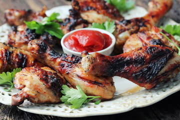 Grilled chicken legs on wooden table served on white plate with coriander