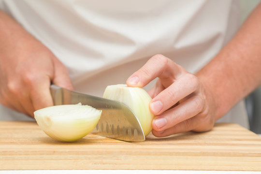 Chef's hands with knife cutting the onion on the wooden board. Preparation for cooking. Healthy eating and lifestyle.