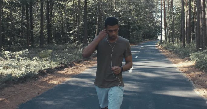 FOLLOW Handsome African American puts on earphones and starts fitness tracking app on his smart watch before jogging. 4K UHD