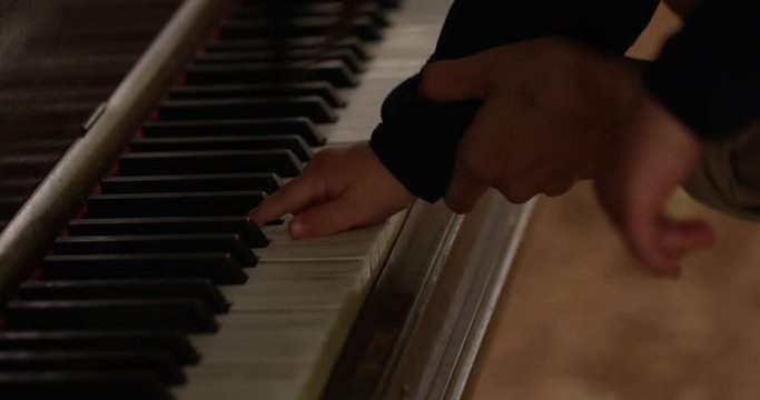 Mother using sons hands to play piano- slow motion up close