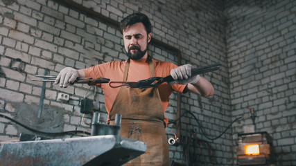 Muscular blacksmith in forge hammering steel products