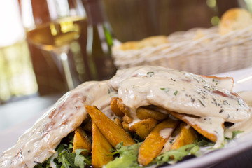 Close up of grilled chicken breast covered with sauce and potatoes in a plate on wooden table. Beautifully served meal at the restaurant. Bread and wine in the background.