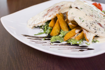 Classy restaurant meal. Grilled chicken breast covered with sauce and potatoes in a plate on wooden table. Beautifully served meal at the restaurant.