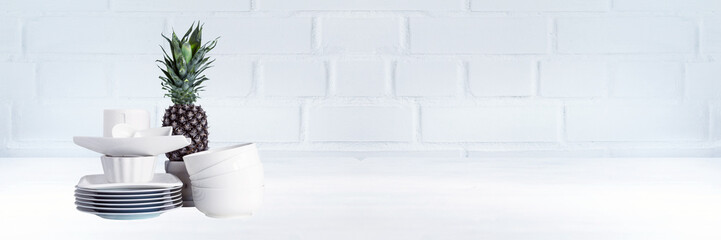 Piece of kitchen interior with white porcelain dishes, kitchen table and pineapple fruit. Copy space. Wide panoramic image.
