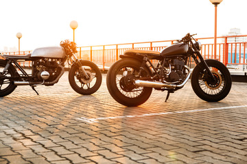 Two vintage custom motorcycle caferacer motorbike looking in same direction on empty rooftop parking lot with backlight sun during sunset. New urban style. Hipster lifestyle.