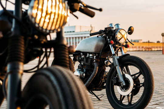 Fototapeta Vintage custom motorcycle cafe racer motorbike with lamp lights turned on. One with grill headlight another with tape cross over optic on empty rooftop parking lot during sunset. Hipster lifestyle.
