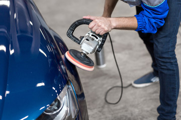 professional mechanic using a power buffer machine for cleaning the body of a car from scratches.