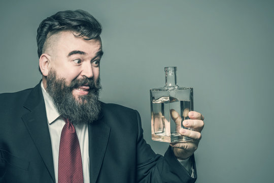 Adult bearded man in suit hungrily looking at a bottle of alcohol. Toned