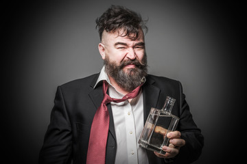 Adult bearded man in suit with a look of disgust on his face holding a bottle of alcohol. Toned