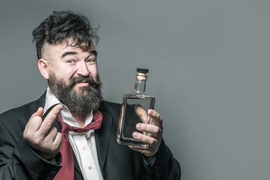 Drunk disheveled bearded man in suit with a bottle of alcohol in his hand showing middle finger on a gray background