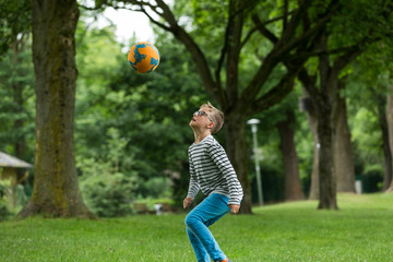Jugendlicher / Heranwachsender / Junge / Kind spielt mit Fussball auf grüner Wiese / Wald