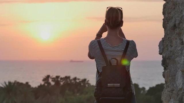 Female traveler with backpack taking photo of sunset sea on her phone