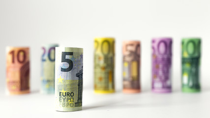 Gerollter 5 Euro Schein mit anderen Geldscheinen im Hintergrund