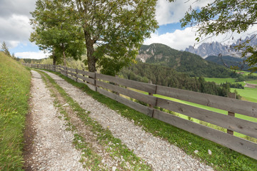 Fototapeta premium Wooden fence long a secondary mountain white street in Val di Funes