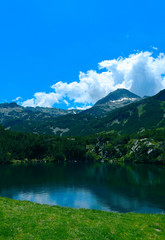 Beautiful mountains lake with a reflection of the high green mountains peaks, on the blue sky background. Amazing Mountain hiking paradise landscape with a lake, no people.