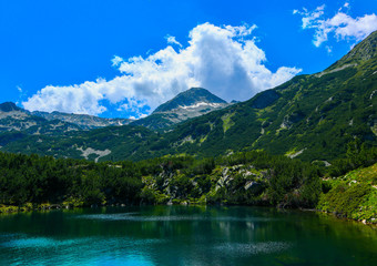 Naklejka na ściany i meble Beautiful mountains lake with a reflection of the high green mountains peaks, on the blue sky background. Amazing Mountain hiking paradise landscape with a lake, no people.