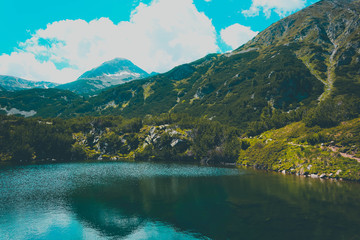 Beautiful mountains lake with a reflection of the high green mountains peaks, on the blue sky background. Amazing Mountain hiking paradise landscape with a lake, no people.