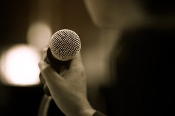 blurred of businessman hand holding microphone for speech presentation in conference hall, vintage tone