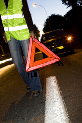 femme en panne de voiture le soir qui pose un triangle de signalement sur la route