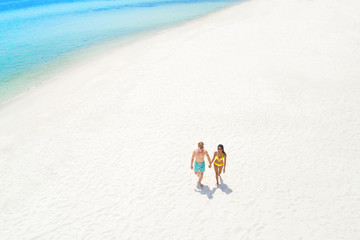 Couple walking on white sand beach in summer, bird eye view