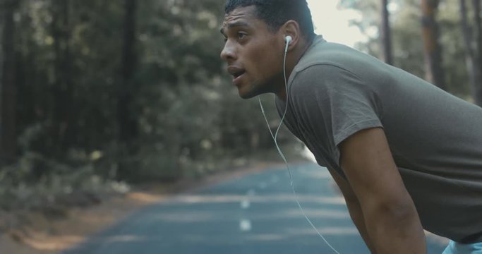 Young fit African American catching breath after jogging on the forest road, turning and smiling into camera. 4K UHD