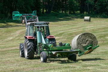 Tractor collecting a roll of haystack in the field