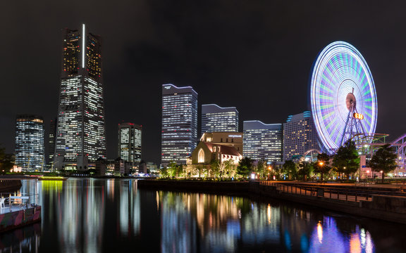 Panoramic photo Yokohama city skyline at night illuminated buildings and ferris wheel are reflected in the ocean water