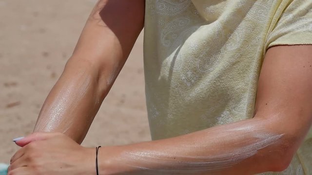 Woman spreading sunscreen on her arm at the beach on a hot sunny day