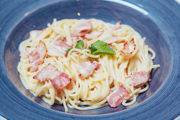 Spaghetti Carbonara with bacon and cheese on blue plate.