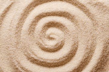 Fototapeta na wymiar Spiral in the sand. Archimedean spiral made with the finger in dry ocherous sand. Macro photo close up from above.