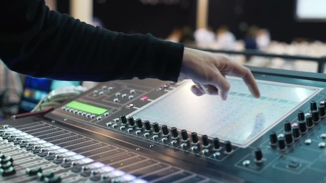 A man is working at an event. audio mixer knobs being pulled up and down by a Director. Hand of the sound producer. Electronics for amplifier and balance of sound in show. Pushes the handle console