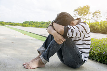 Sad and serious Asain man sitting hug his knee and head down on knee alone in the green garden,...