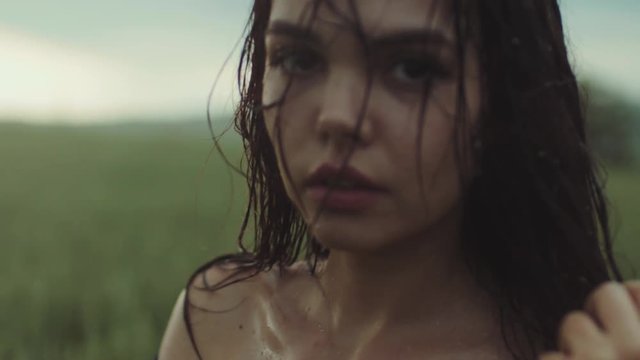 Close up view of a gorgeous young woman with bare shoulders soaked in rain. Rain drops on the beautiful woman&rsquo;s face. Natural beauty, playful mood. Being happy. Slow motion, camera stabilizer shot.